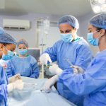 Diverse Team of Professional surgeon, Assistants and Nurses Performing Invasive Surgery on a Patient in the Hospital Operating Room. Surgeons Talk and Use Instruments. Real Modern Hospital.