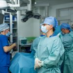 Surgical team readies for procedure. A surgical team in scrubs and masks is preparing for an operation in a modern hospital environment, focused and attentive to their tasks.